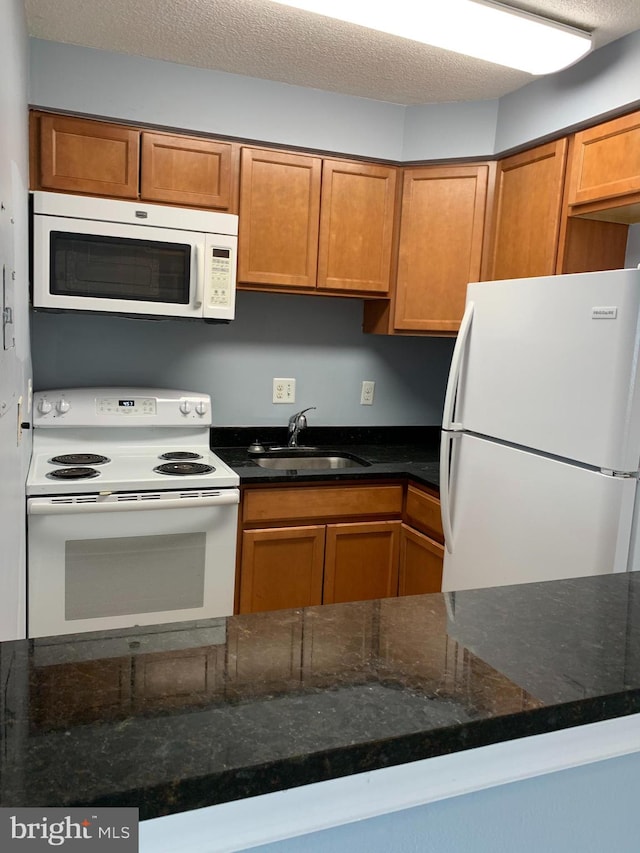 kitchen featuring dark stone counters, white appliances, a textured ceiling, and sink