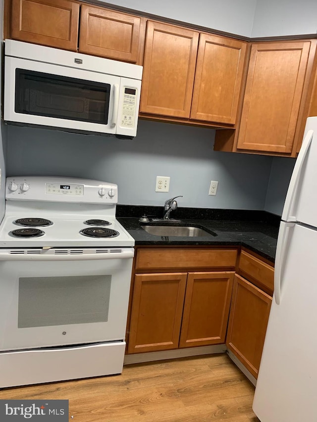 kitchen with sink, white appliances, light wood-type flooring, and dark stone countertops