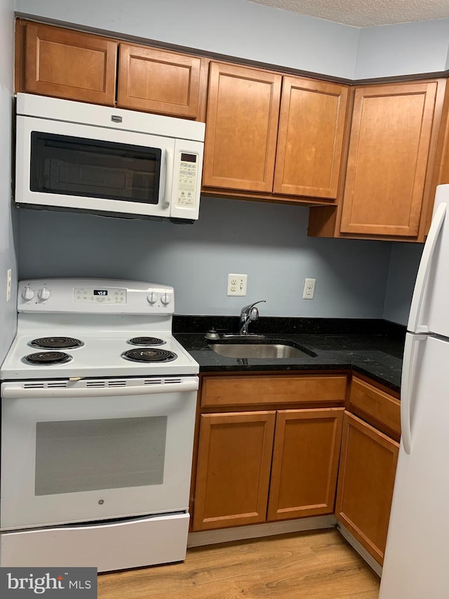 kitchen with dark stone counters, light hardwood / wood-style flooring, white appliances, and sink