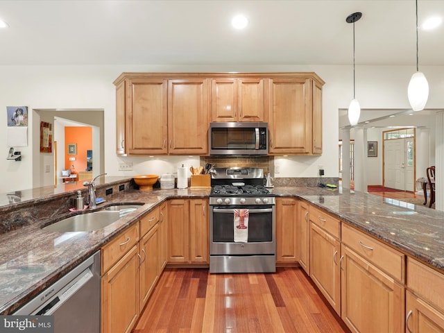 kitchen with stainless steel appliances, dark stone countertops, decorative light fixtures, sink, and light hardwood / wood-style flooring