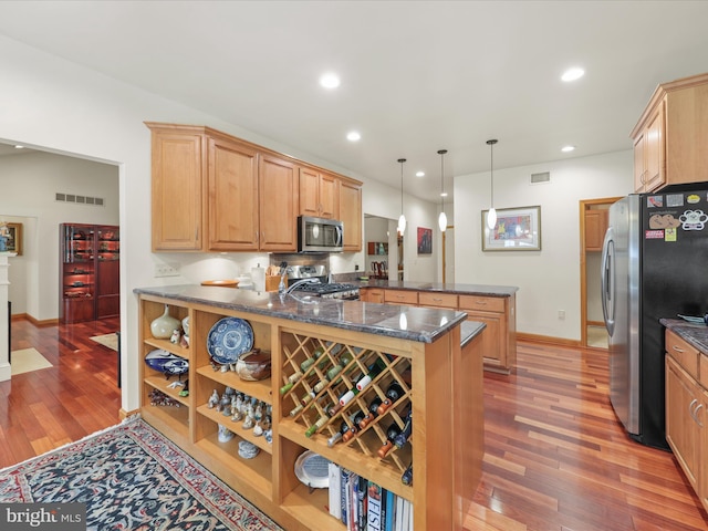 kitchen with kitchen peninsula, hardwood / wood-style floors, appliances with stainless steel finishes, hanging light fixtures, and dark stone countertops