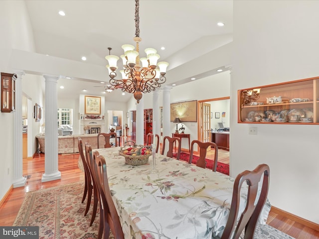 dining space with light wood-type flooring, a notable chandelier, decorative columns, and a raised ceiling