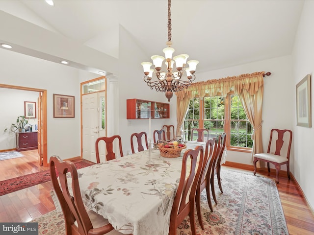 dining space featuring ornate columns, vaulted ceiling, a chandelier, and light wood-type flooring