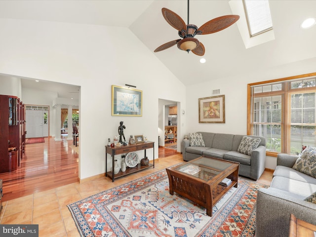 living room featuring a skylight, light hardwood / wood-style floors, ceiling fan, and high vaulted ceiling