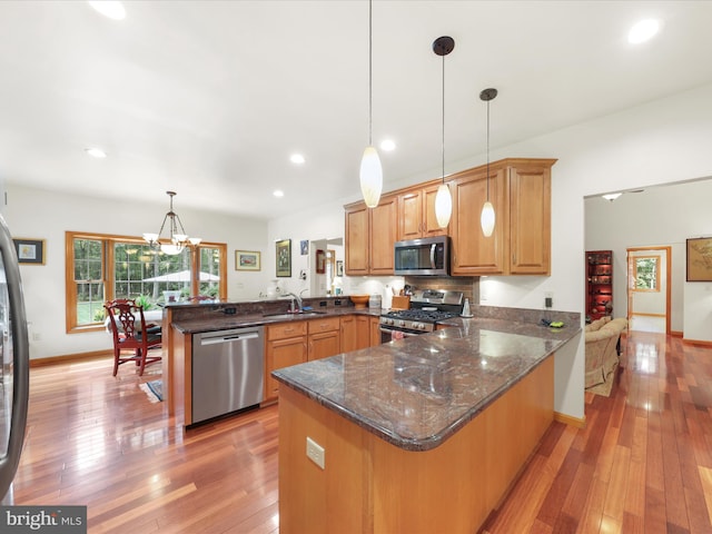 kitchen featuring appliances with stainless steel finishes, decorative light fixtures, kitchen peninsula, a chandelier, and light hardwood / wood-style flooring