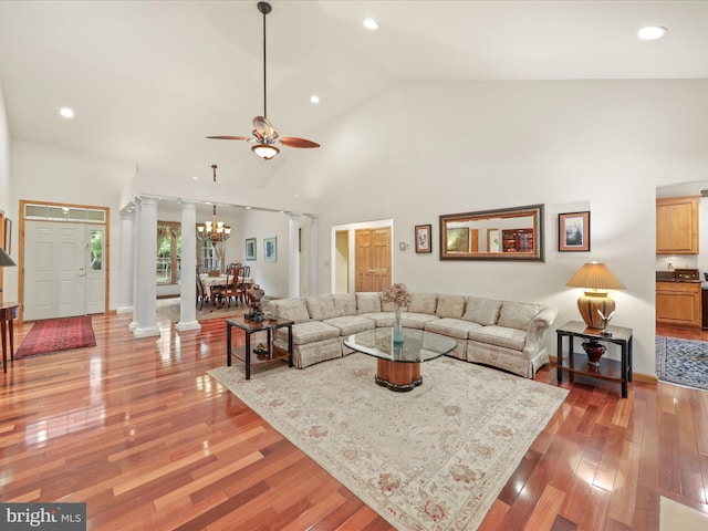 living room featuring wood-type flooring, high vaulted ceiling, ornate columns, and ceiling fan with notable chandelier