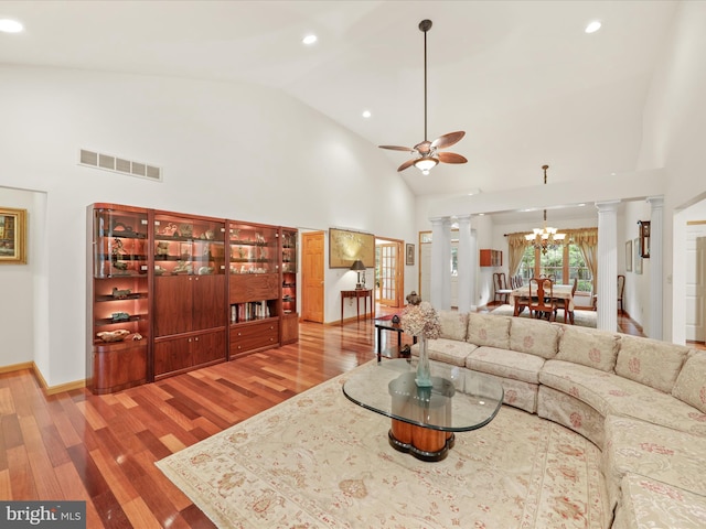 living room featuring ceiling fan with notable chandelier, high vaulted ceiling, wood-type flooring, and ornate columns