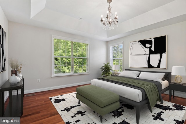 bedroom featuring an inviting chandelier, dark hardwood / wood-style floors, and a tray ceiling