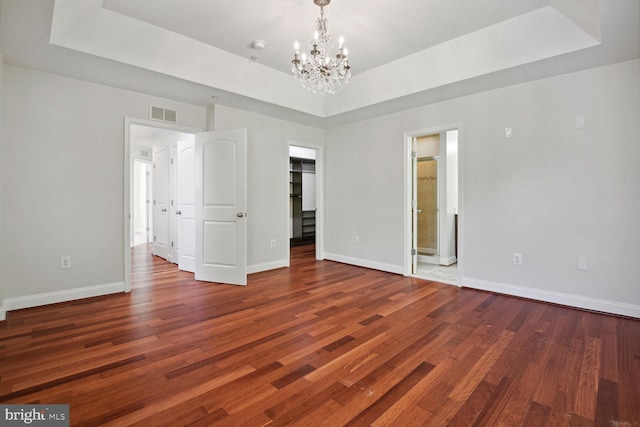 unfurnished room featuring an inviting chandelier, dark wood-type flooring, and a raised ceiling