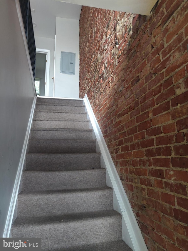 staircase featuring electric panel and brick wall