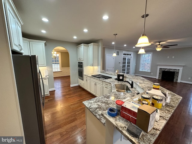 kitchen featuring a sink, a high end fireplace, stainless steel appliances, arched walkways, and a peninsula