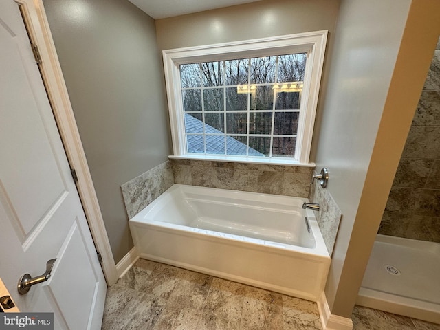 bathroom featuring baseboards, plenty of natural light, a bath, and a shower stall