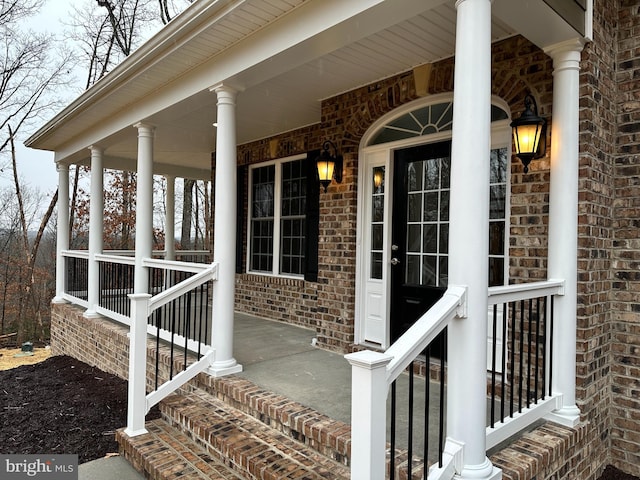 view of exterior entry featuring brick siding and covered porch