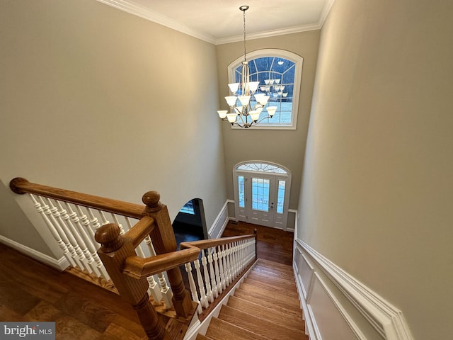 stairs featuring an inviting chandelier, wood finished floors, baseboards, and ornamental molding