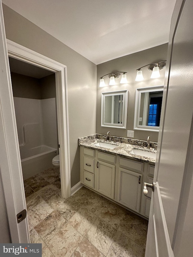 bathroom featuring double vanity, toilet, baseboards, and a sink