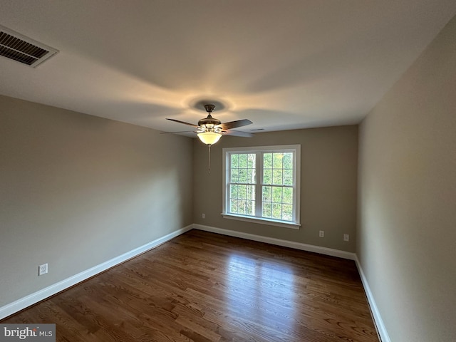 spare room with a ceiling fan, dark wood-style floors, visible vents, and baseboards