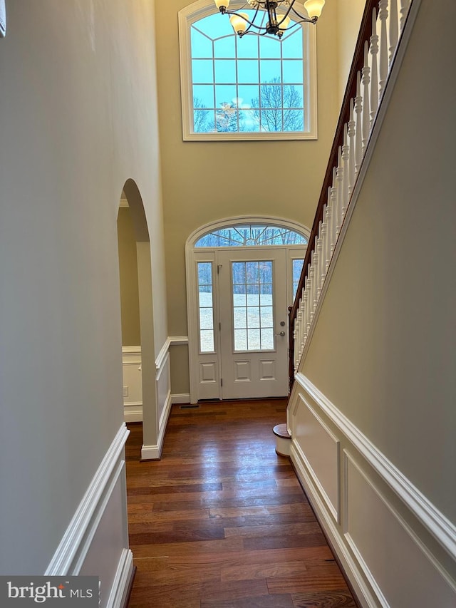 entrance foyer with dark wood-type flooring, a notable chandelier, stairway, arched walkways, and a decorative wall