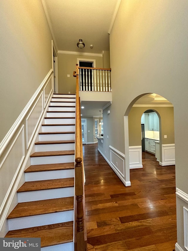 stairs featuring ornamental molding, wainscoting, wood finished floors, arched walkways, and a decorative wall