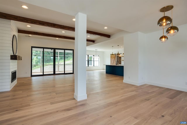 unfurnished living room featuring a large fireplace, light hardwood / wood-style flooring, an inviting chandelier, and beamed ceiling