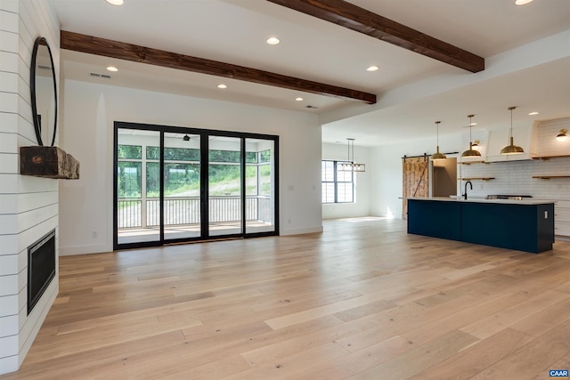 unfurnished living room featuring an inviting chandelier, light wood-type flooring, a fireplace, sink, and beam ceiling