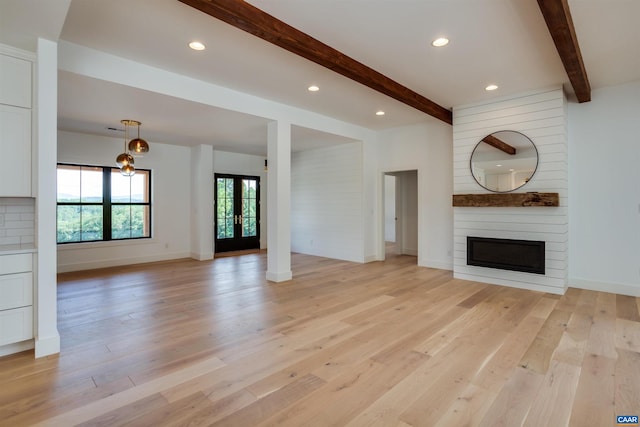 unfurnished living room featuring a large fireplace, beam ceiling, french doors, and light hardwood / wood-style flooring