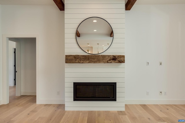 room details featuring beamed ceiling, a large fireplace, and light hardwood / wood-style flooring