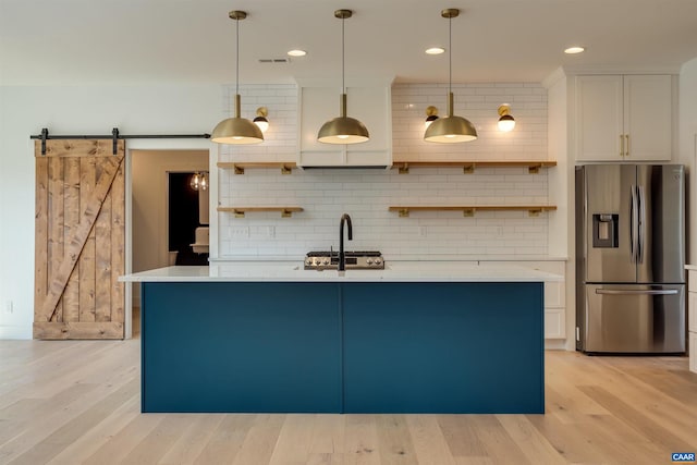 kitchen featuring pendant lighting, a barn door, light hardwood / wood-style flooring, white cabinetry, and stainless steel fridge