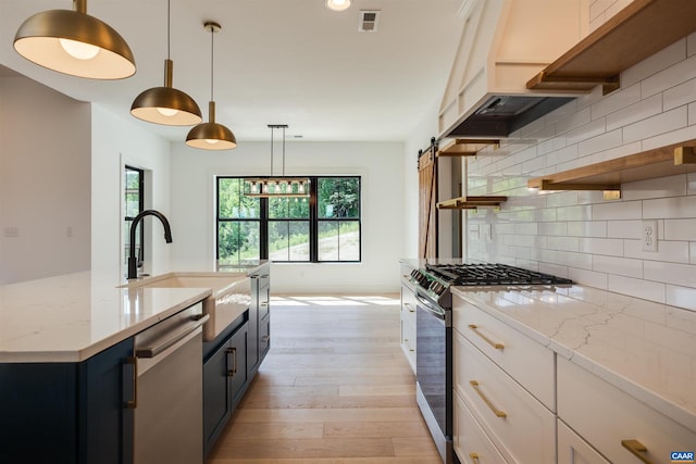 kitchen with white cabinetry, a barn door, appliances with stainless steel finishes, light wood-type flooring, and tasteful backsplash