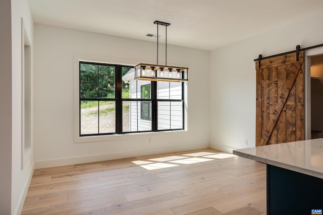 unfurnished dining area with a barn door and light hardwood / wood-style flooring