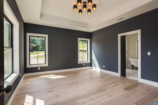 unfurnished room with a raised ceiling, a notable chandelier, light wood-type flooring, and a wealth of natural light