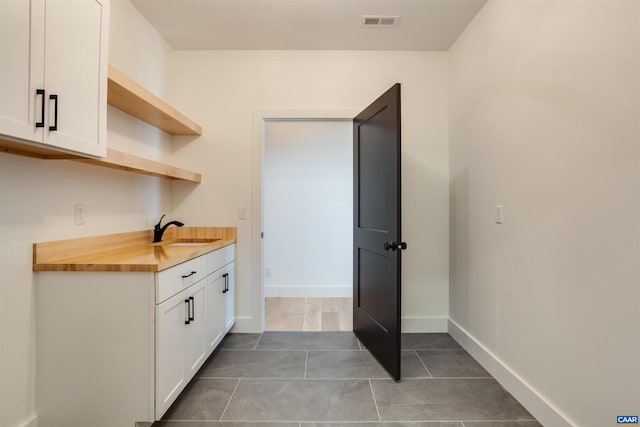 kitchen featuring white cabinets, dark tile flooring, sink, and wood counters