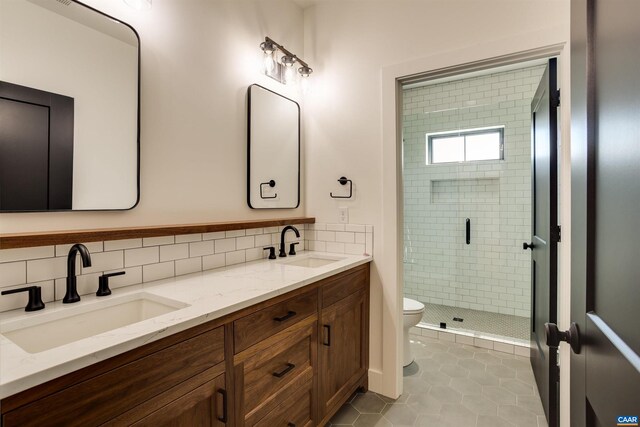 bathroom featuring toilet, double sink vanity, a shower with door, backsplash, and tile flooring