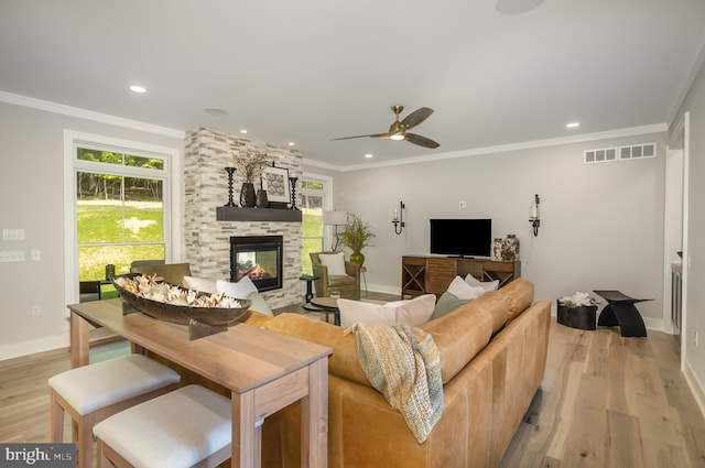 living room with ceiling fan, ornamental molding, light wood-type flooring, and a stone fireplace