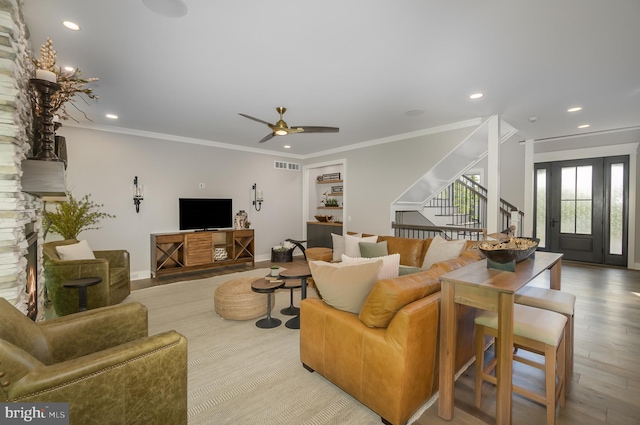 living room with light hardwood / wood-style flooring, ornamental molding, a stone fireplace, and ceiling fan