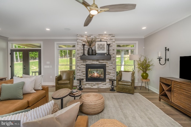 living room featuring ceiling fan, ornamental molding, hardwood / wood-style floors, and a stone fireplace