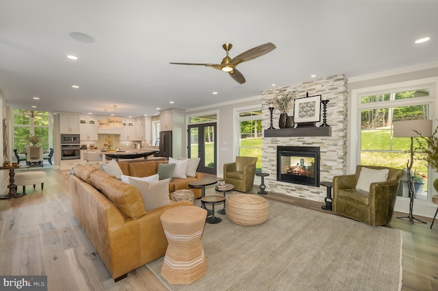 living room with a fireplace, plenty of natural light, ceiling fan, and light wood-type flooring