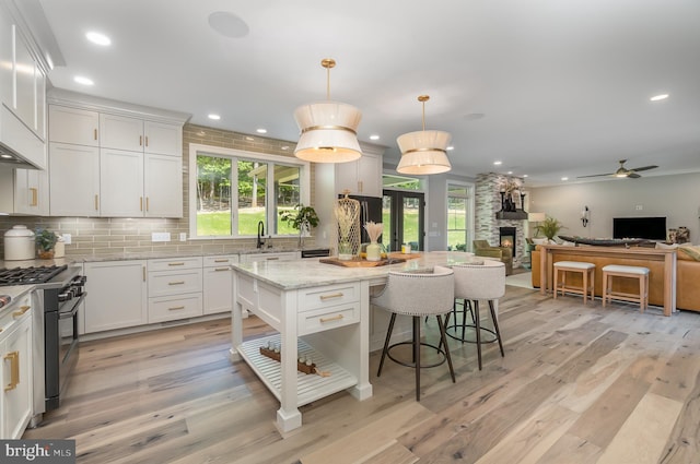 kitchen with ceiling fan, a fireplace, light stone countertops, tasteful backsplash, and light wood-type flooring