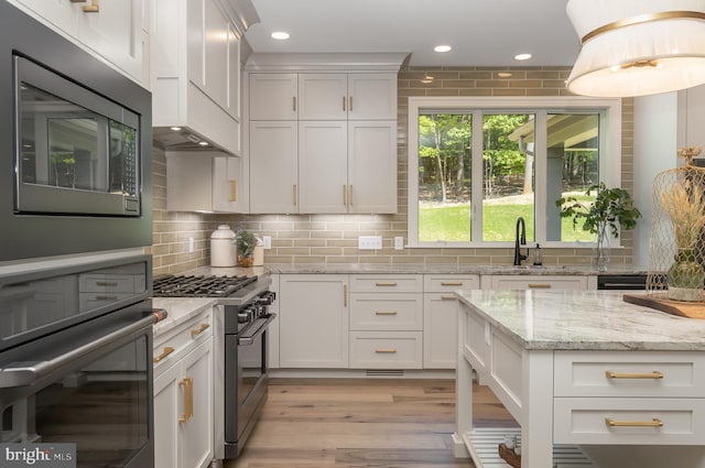 kitchen with light stone counters, tasteful backsplash, stainless steel appliances, custom exhaust hood, and light wood-type flooring