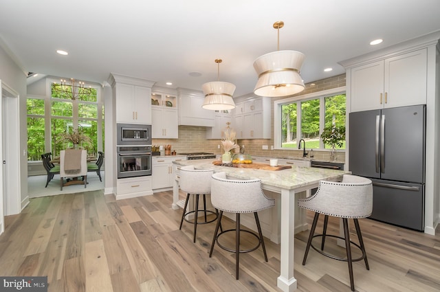 kitchen featuring stainless steel appliances, a kitchen island, decorative light fixtures, tasteful backsplash, and light wood-type flooring