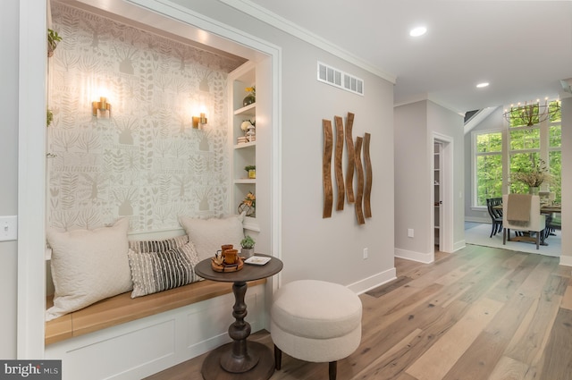 living area with built in shelves, a chandelier, ornamental molding, and light hardwood / wood-style flooring