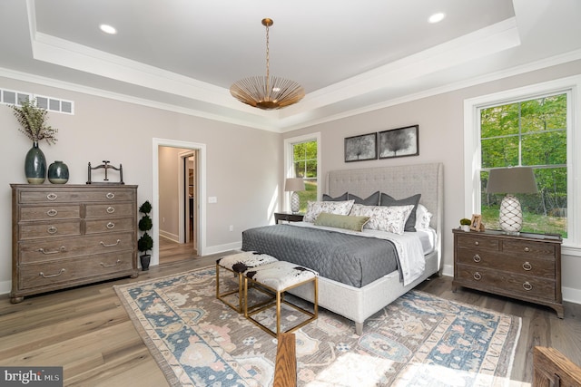 bedroom with a raised ceiling, crown molding, and light wood-type flooring