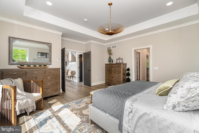 bedroom featuring ornamental molding, light wood-type flooring, and a raised ceiling