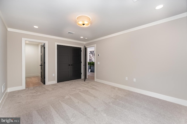 unfurnished bedroom with light colored carpet, ornamental molding, and a walk in closet