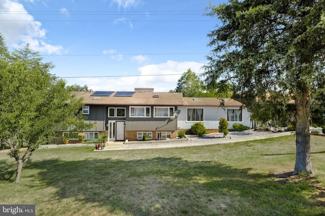 rear view of property featuring a yard and solar panels