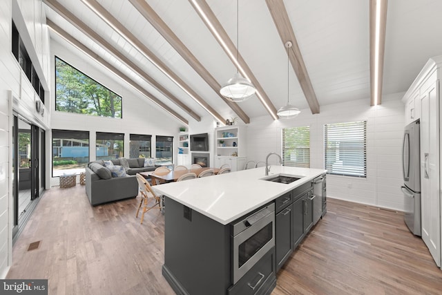 kitchen with stainless steel appliances, decorative light fixtures, a kitchen island with sink, dark hardwood / wood-style floors, and sink