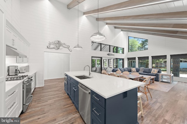 kitchen with appliances with stainless steel finishes, white cabinetry, high vaulted ceiling, blue cabinetry, and pendant lighting