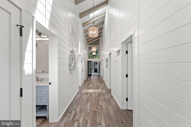 hall featuring wood-type flooring, beamed ceiling, wooden walls, and high vaulted ceiling