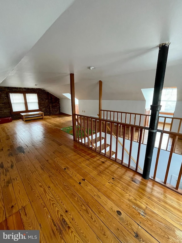 stairway with lofted ceiling, brick wall, and light wood-type flooring