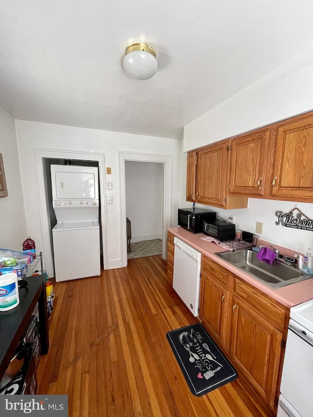 kitchen featuring white dishwasher, range, light wood-type flooring, stacked washer and clothes dryer, and sink