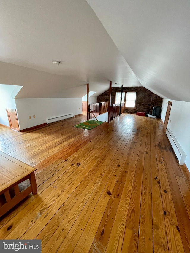 interior space with brick wall, baseboard heating, lofted ceiling, and light hardwood / wood-style flooring